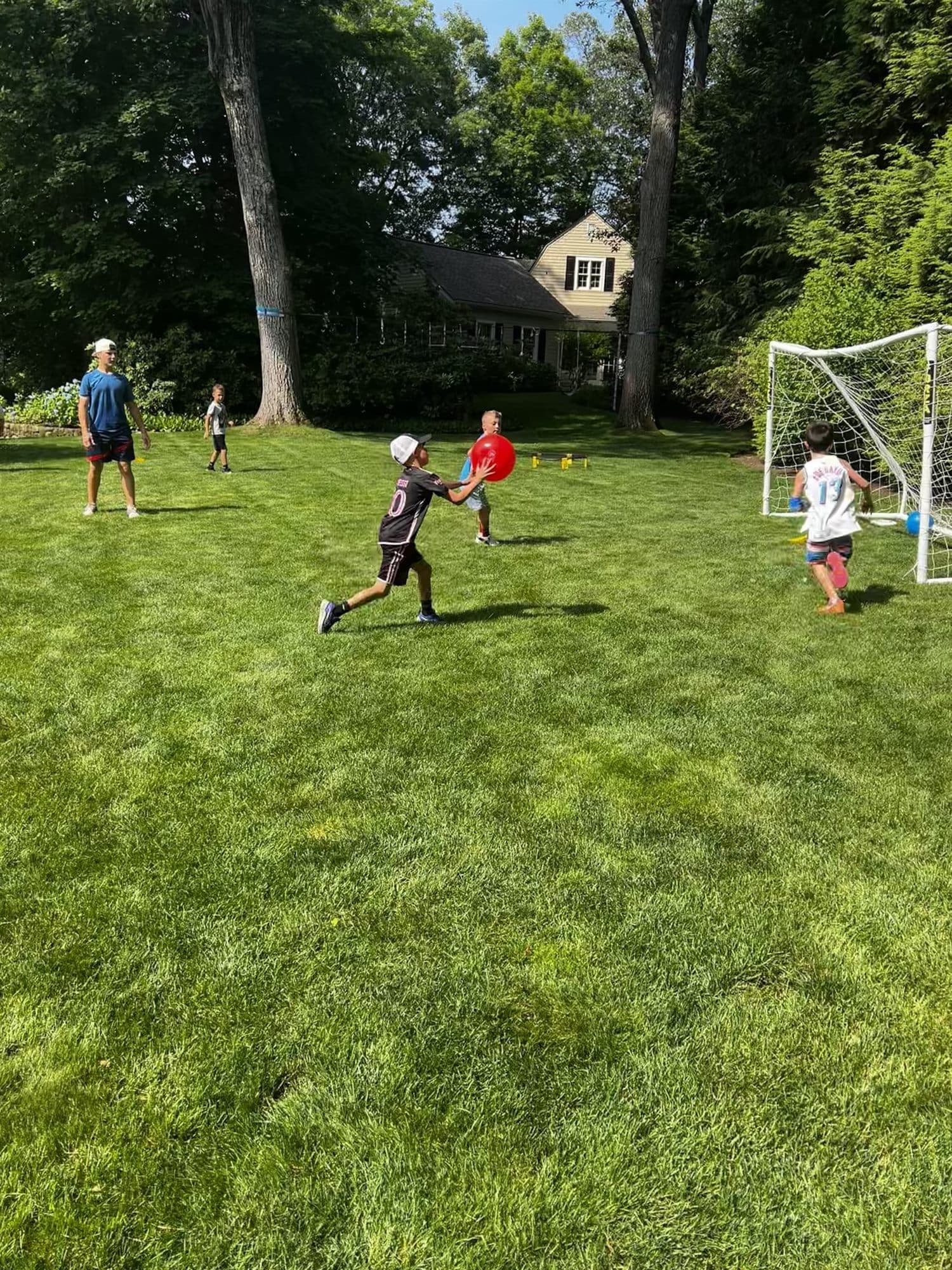 Campers running across a wide green lawn toward a goal, with a coach off to the side.