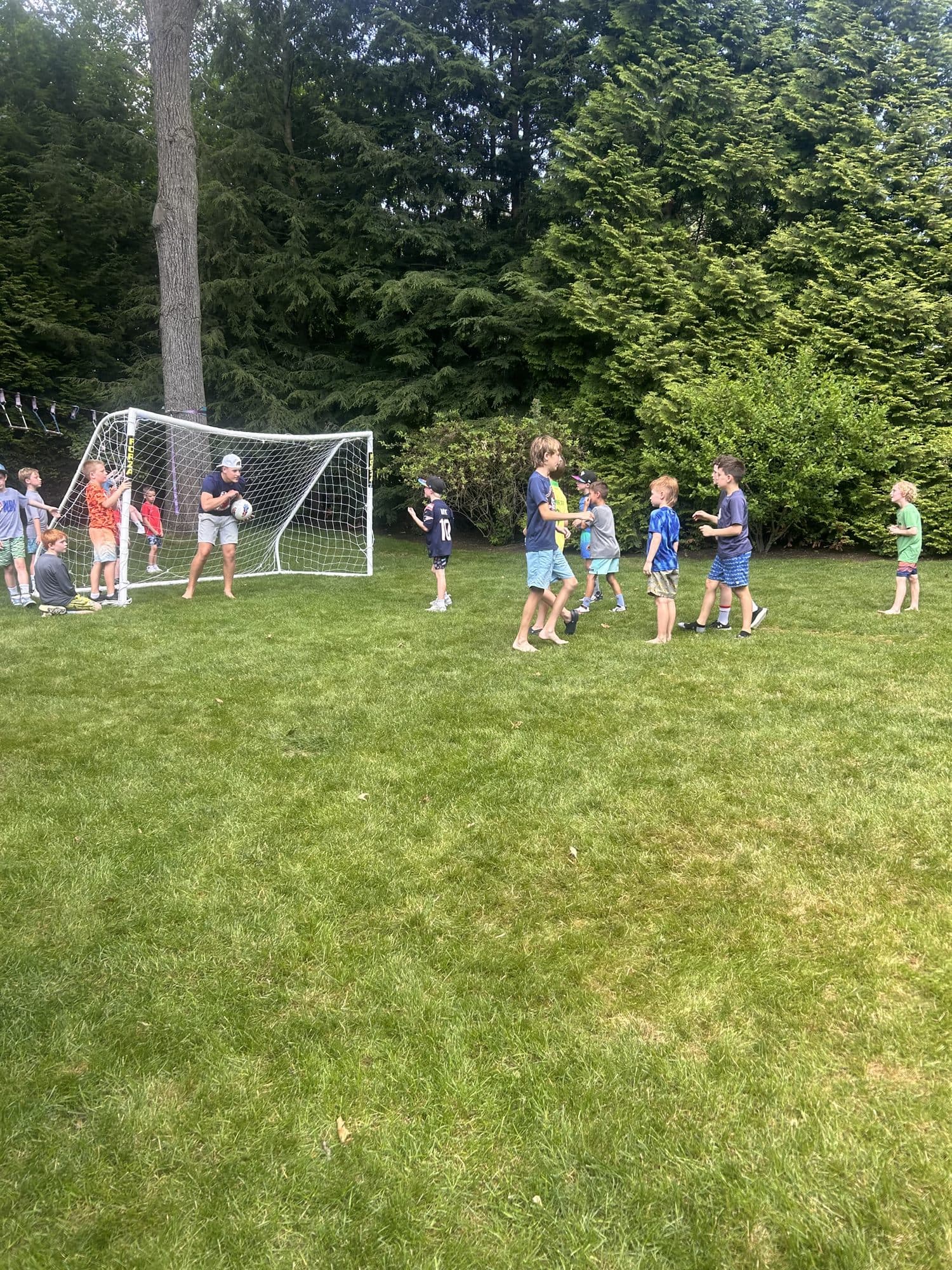 Campers spread across the grass in front of a soccer goal while a coach holds the ball.