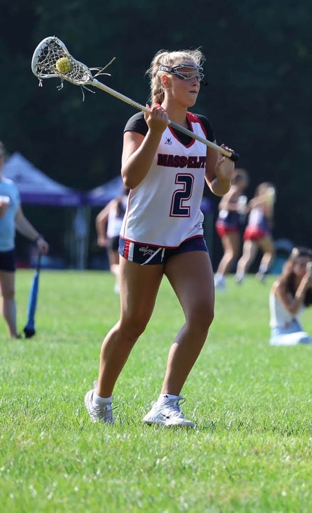 Lawson Andrews on the lacrosse field in a white Mass Elite uniform, number 2, cradling the ball in her stick.